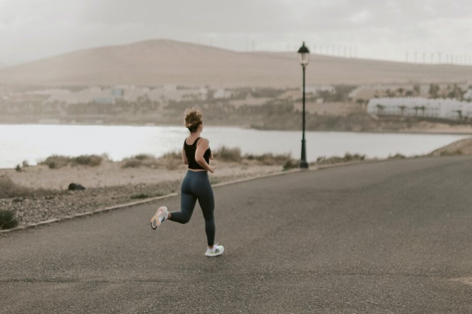 hardlopen woman in black tank top and white pants running on gray asphalt road during daytime