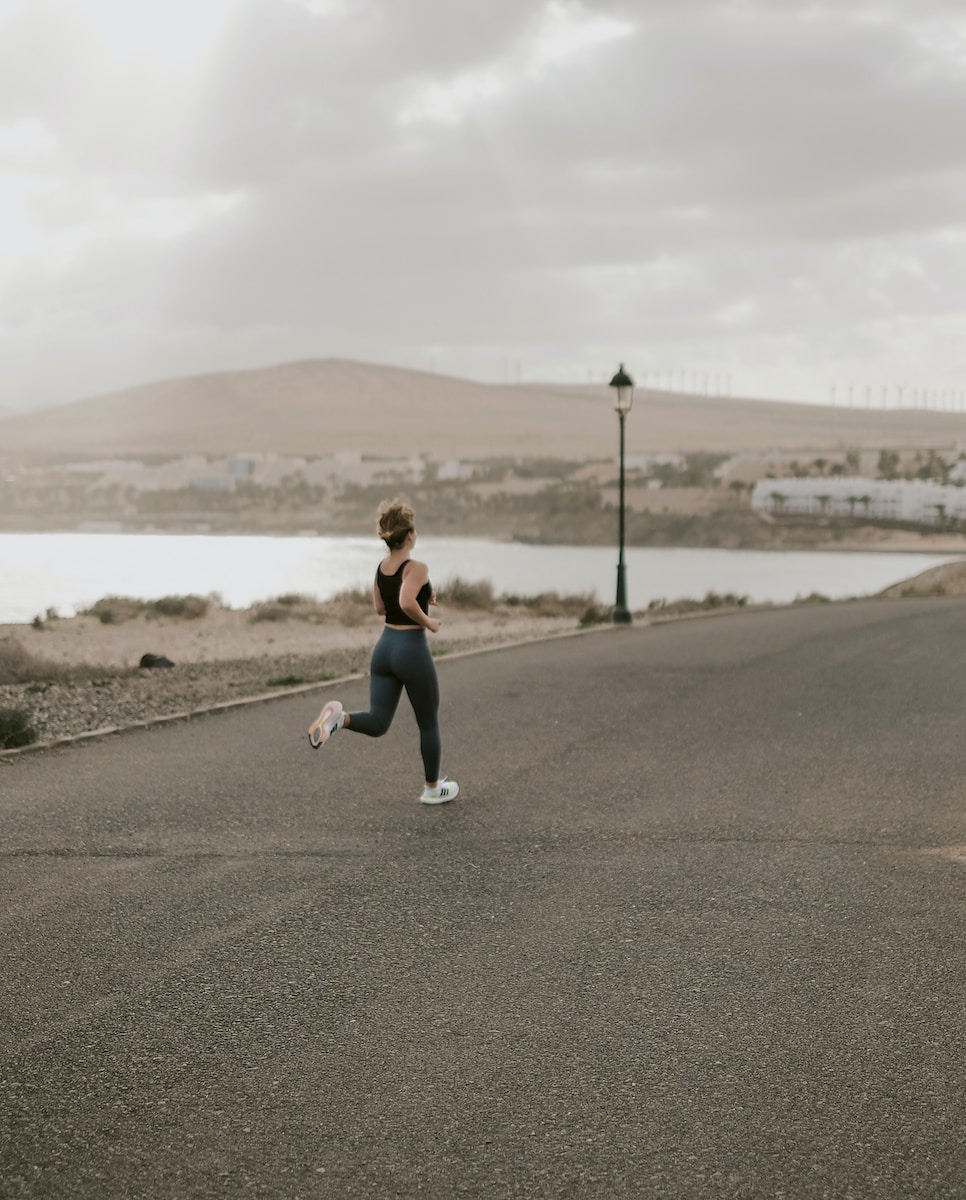 hardlopen woman in black tank top and white pants running on gray asphalt road during daytime